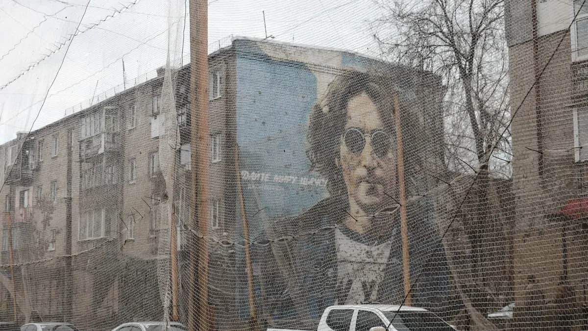 A John Lennon mural saying ‘Give Peace a Chance’ on a wall behind anti-drone nets in the city of Izyum, in northeastern Ukraine’s Kharkiv region, 12 December 2025. Photo: EPA / SERGEY KOZLOV